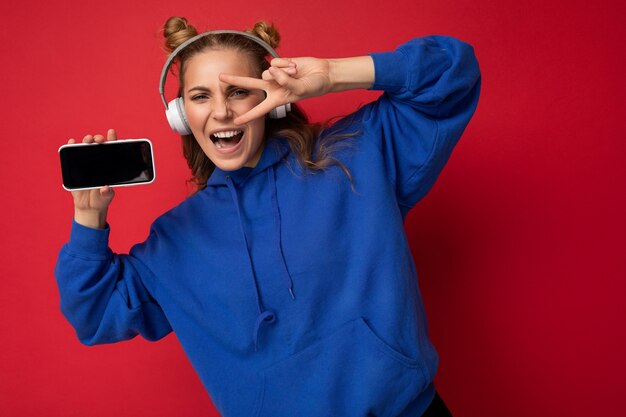 Photo of beautiful positive happy funny young woman wearing stylish blue hoodie isolated over red