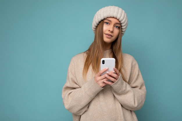 Photo of beautiful positive young blonde woman wearing stylish beige warm sweater and knitted winter