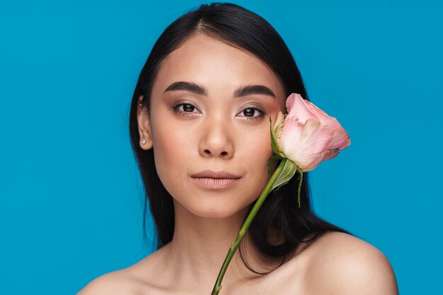 Photo of a beautiful pretty asian young woman posing isolated on blue wall with flower.