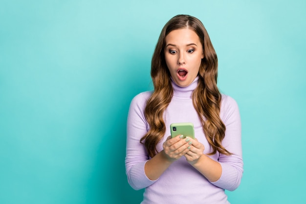 Photo of beautiful shocked lady open mouth hold telephone hands reading blog post awful negative comments wear purple violet turtleneck isolated teal pastel blue color