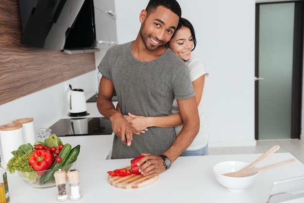 Photo of beautiful young couple in the kitchen hugging while cooking.