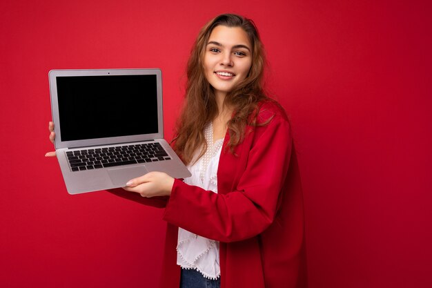 カラフルな背景で隔離のカメラを見ているコンピュータのラップトップを保持している美しい少女の写真。切り取る