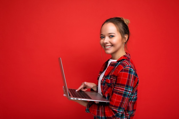 화려한 배경 위에 격리된 카메라를 보고 있는 컴퓨터 노트북을 들고 있는 아름다운 소녀의 사진.