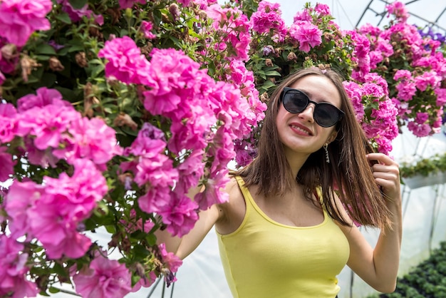 Photo of beautiful young girl posing between flowers in a greenhouse. Lifestyle