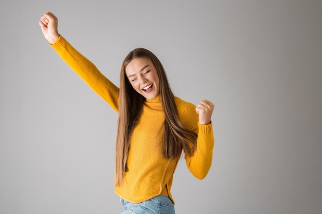 Photo of a beautiful young happy woman isolated over grey wall showing winner gesture