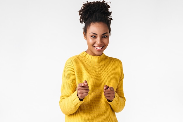 Photo of a beautiful young happy woman posing over white wall pointing to you.