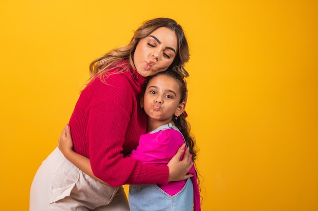 Photo of a beautiful young mommy holding her arms hugging her little daughter good mood adorable sincere heart feelings in the back jeans t-shirts isolated with yellow color background