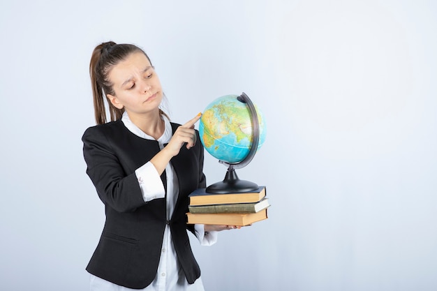 Photo of beautiful young teacher with books pointing at globe on white.