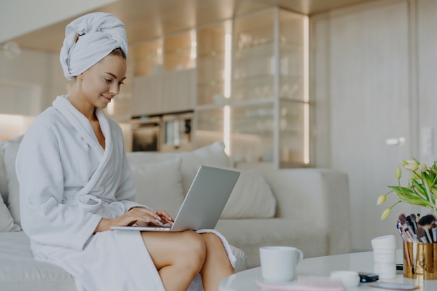 Photo of beautiful young woman in bathrobe types on laptop computer