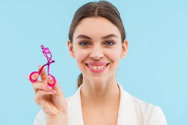 Photo of beautiful young woman posing isolated holding lash curler doing makeup.