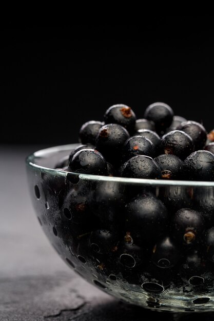 Photo of black currant in glass transparent cup on black empty wall