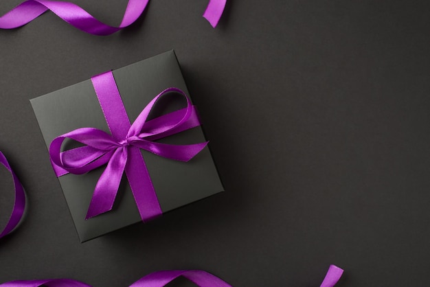 黒い背景に分離された弓として包まれた紫色のリボンが付いた黒いギフトボックスの写真の上