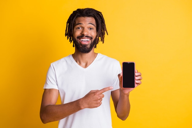 Photo of black guy beard dreadlocks indicate finger hold showing telephone touchscreen empty space wear white t-shirt isolated yellow color background