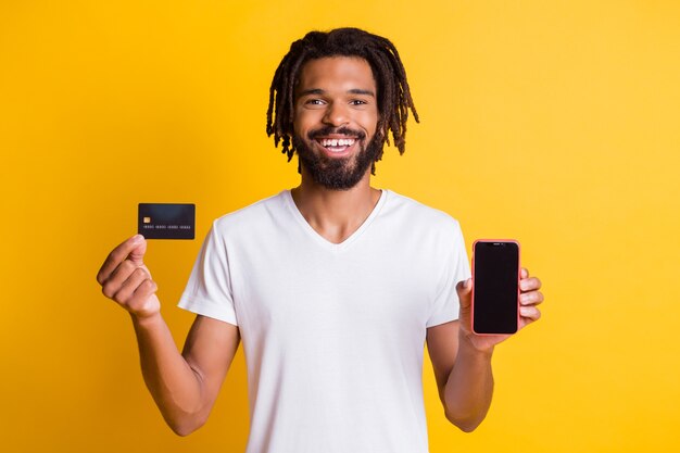 Photo of black guy hold presenting debit card telephone screen empty space wear white t-shirt isolated yellow color background