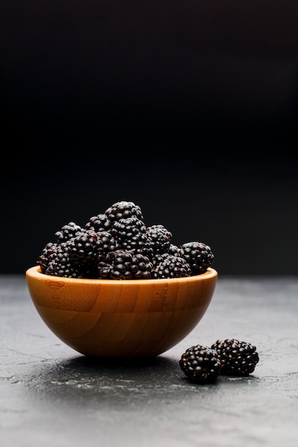 Photo of blackberry in wooden cup on empty black background in studio