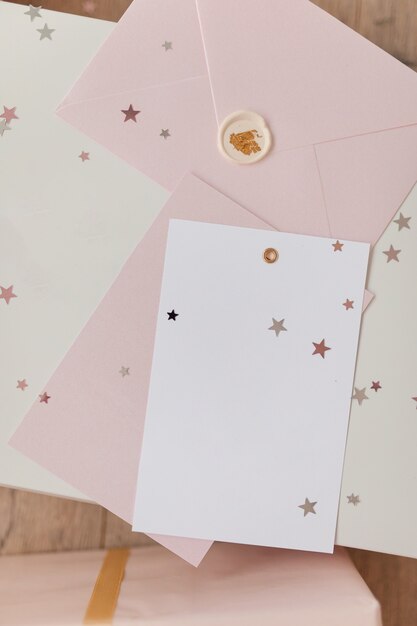 Photo of Blank white card in pink envelope isolated woodden color background with glitter stars, vaucher, gift certificate. White and pink background