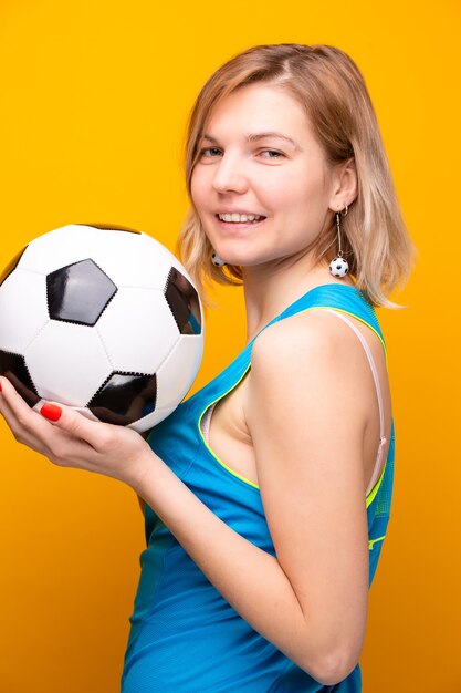 Photo of blonde with soccer ball on yellow background in studio