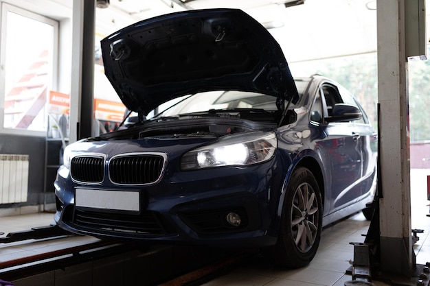 Photo of a blue passenger car at the service station under repair with an open hood and headlights