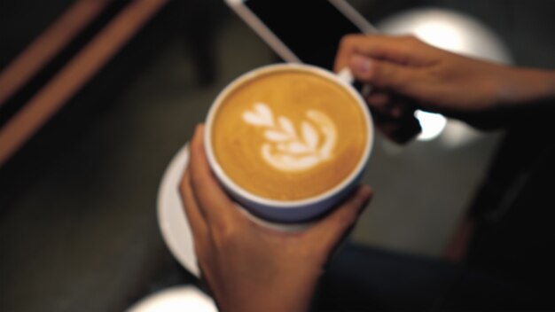 Photo blurred of woman hand holding the latte art on top in coffee cups at the coffee shop