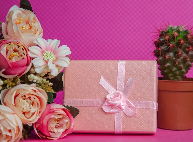 A photo of a bouquet of flowers a gift in the form of a box and a cactus on a pink background front