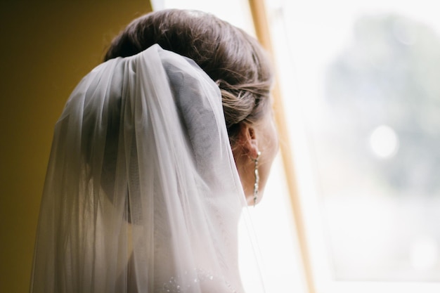 Photo photo of the bride from the back close-up, wedding white veil, the bride is standing by the window