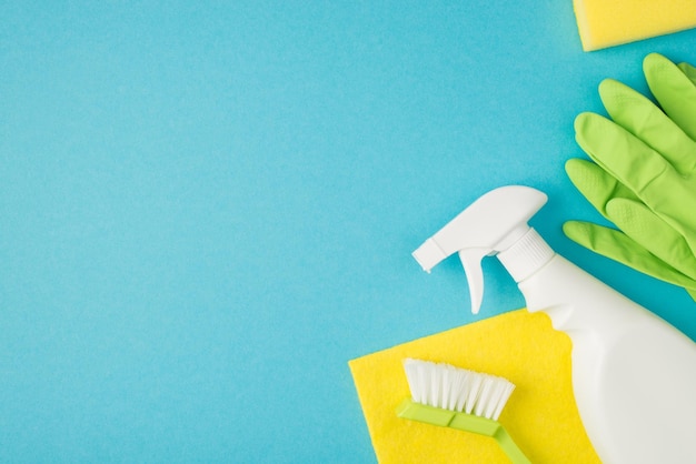 Above photo of brush spray cleaning rag soap and green gloves isolated on the blue background