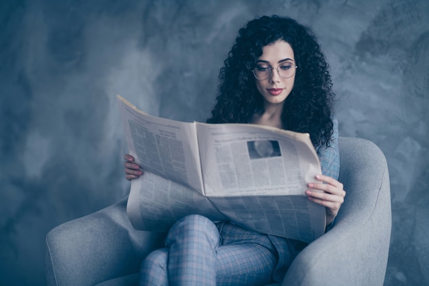 Photo of business lady sit in chair read digest news isolated over concrete wall