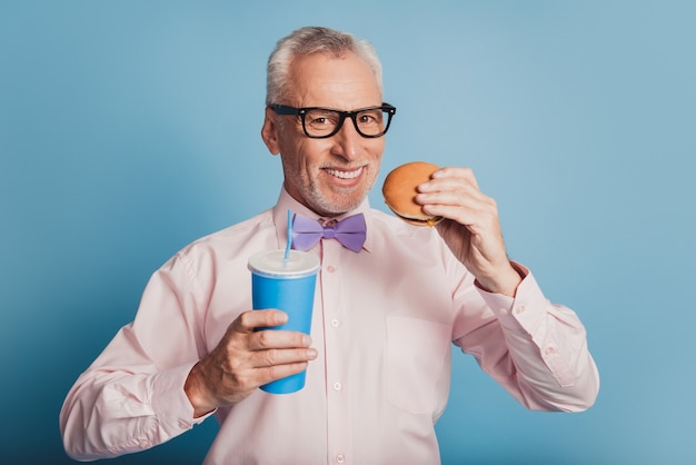 Фотография делового человека, едящего гамбургер с содовой сладкой водой, изолировала синий фон