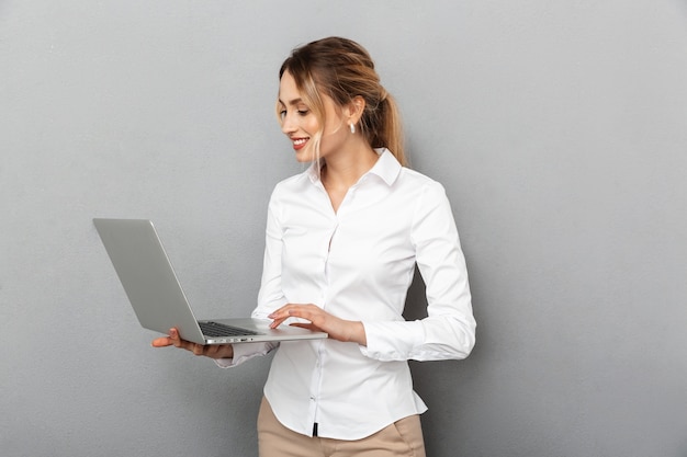 Foto di donna d'affari in abbigliamento formale in piedi e tenendo il computer portatile in ufficio, isolato