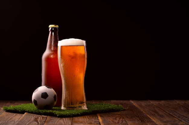 Photo of buttle and glass of beer soccer ball on green grass