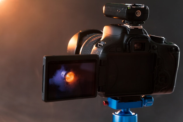 Photo of the camera on a blue tripod that photographs in the studio a professional lighting device in the smoke. Studio lights and smoke equipment. Advertising photo session of the lighting device