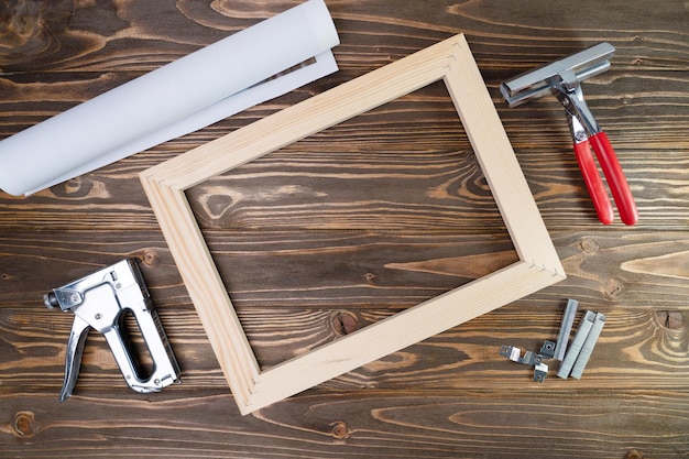 Photo on canvas in roll, canvas stretcher, stapler and stretching tool on brown wooden background