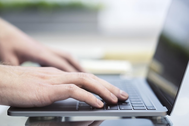 The photo captures a closeup of male hands busily typing on a cuttingedge laptop with a blurred office scene serving as the backdrop