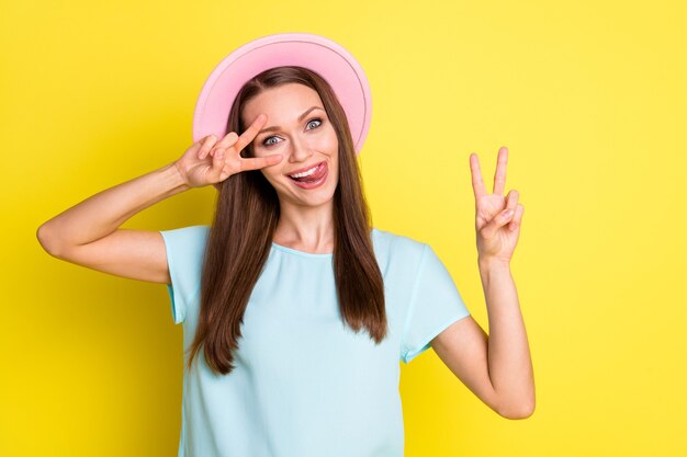 Photo of careless playful girl have free time holiday make v-sign lick tongue lips teeth wear blue pink hat clothes isolated over bright shine color background