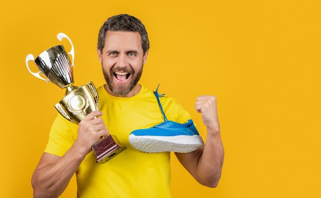 Photo of champion man hold award and sneakers banner champion man hold award isolated on yellow champion man hold award on background champion man hold award in studio