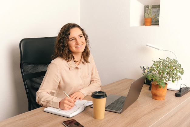 Photo of charming young woman writing in planner at office desk