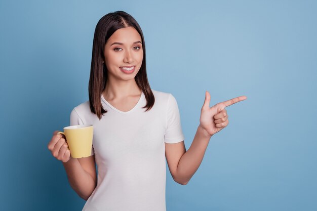 Photo of cheerful adviser lady hold cup indicate finger empty space promoting sale on blue background