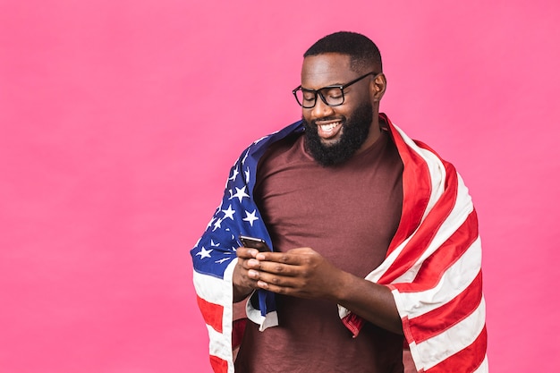 Photo of cheerful american african man protester raise american\
national flag black people revolution love all human beings express\
unity solidarity isolated over pink background. using mobile\
phone.