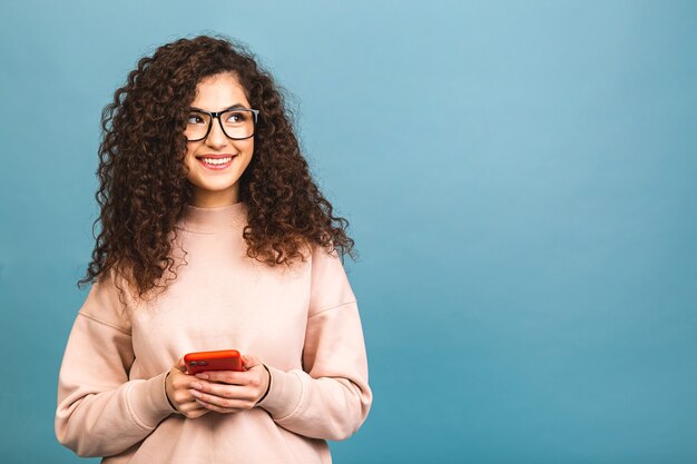 Photo of cheerful cute beautiful young woman chatting by mobile phone isolated over blue wall background.