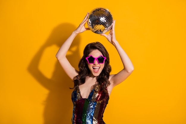 Photo of cheerful energetic party girl hold glitter glowing disco ball enjoy rejoice dance night club wear glossy skirt star shape spectacles isolated over vivid color background