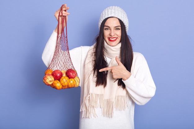 Photo of cheerful good looking adorable young woman holding handbag with fruit