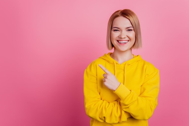 Photo of cheerful lovely blonde lady indicate finger empty space wear white t-shirt isolated on pink background