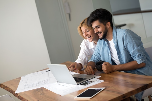 Photo of cheerful loving young couple using laptop and analyzing their finances with documents