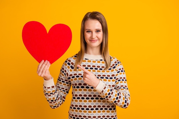 Photo of cheerful nice happy young woman hold hands heart shape isolated on yellow color background