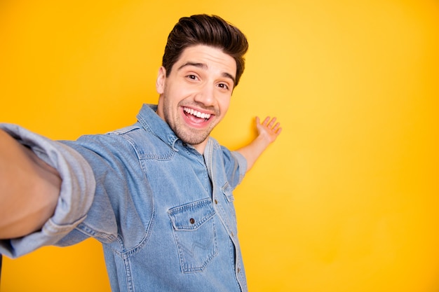 Photo of cheerful positive attractive man welcoming you to come to empty space behind him taking selfie isolated vivid color wall