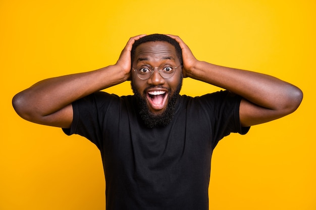 Photo of cheerful positive funny cute black man overjoyed about discounted shopping mall grabbing his head with hands in t-shirt isolated vibrant color yellow wall