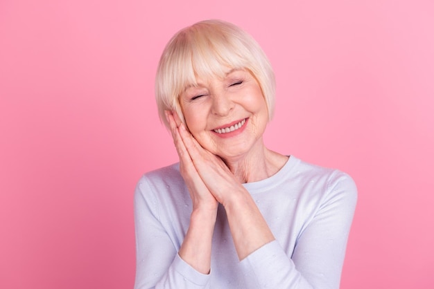 Photo of cheerful senior lady arms touch cheek sleep dream rest bedtime isolated over pink color background