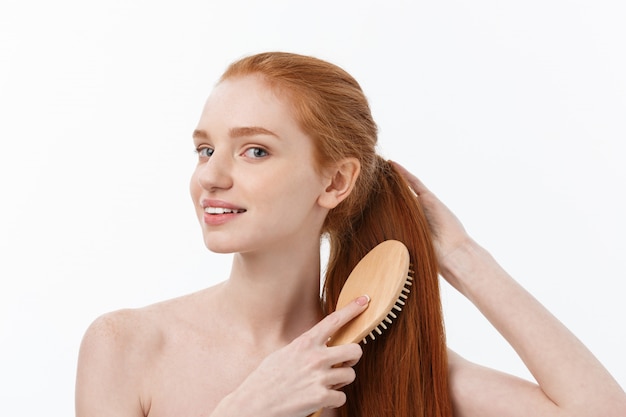 Photo of cheerful smiling freckled ginger young woman combs her long red hair