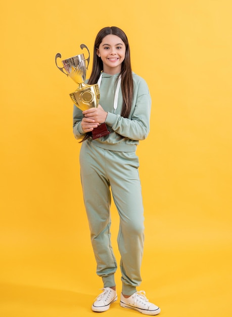 Фото веселой девушки-чемпиона-подростка с золотым кубком. Девушка-чемпионка, изолированная на желтом.
