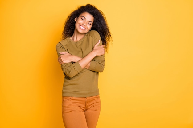 鮮やかな色の背景の上に分離された彼女の新しく購入したセーターを楽しんでいるオレンジ色のズボンのズボンを身に着けている陽気な歯を見せるかわいい素敵な魅力的な魅力的な黒人女性の写真